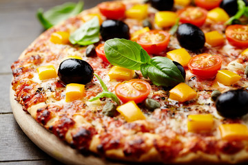 Tasty pizza with cherry tomatoes, mozzarella cheese, black olives, orange pepper, capers and fresh basil. 