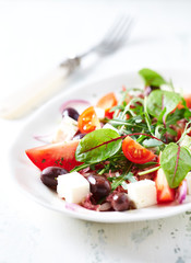 Tasty and healthy salad with various tomatoes, feta cheese, kalamata olives and fresh herbs on white wooden background. Close up. 
