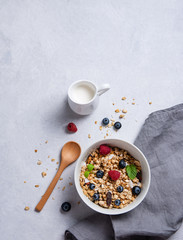 sweet muesli with berries in plate with coconut milk on gray  table.