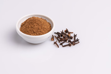 Ground cloves in white ceramic bowl isolated on white background, soft light, studio shot, copy space.Whole cloves.