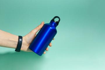 Close-up of female hand holding a reusable, aluminium thermal water bottle of phantom blue color,...