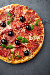 Pizza with salami, black olives and fresh herbs. Home made food. Concept for a tasty and hearty meal. Dark stone background. Top view. 
