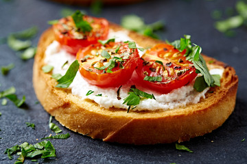 Crostini withe cream cheese, cherry tomatoes and fresh basil. Dark stone background. Close up. 