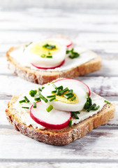 Tasty sandwiches with cream cheese, radish, egg and chive. Bright wooden background. Close up. 