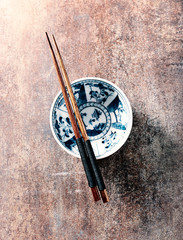 Empty ceramics bowl and wooden chopsticks on rustic background. Top view. Copy space. 