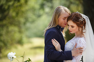 Young Bride and Groom couple in a summer garden. Tender holding each other. Redhead woman and blonde man with long hairs. Young family outdoor in nature. Love and tenderness