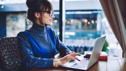 Positive female software developer working remotely in comfortable cafeteria with great public internet connection using application for programming on laptop computer, concept of distance job