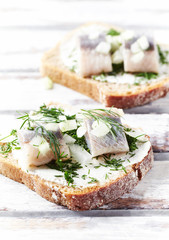 Tasty sandwiches with cream cheese, salted herring and fresh herbs. Bright wooden background. Close up. 