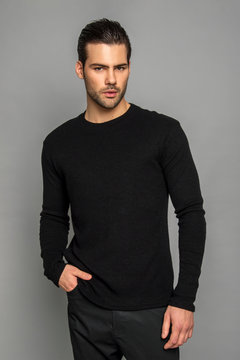 Muscle strong beautiful stripped male model in black jamper and black trousers on grey isolated font background