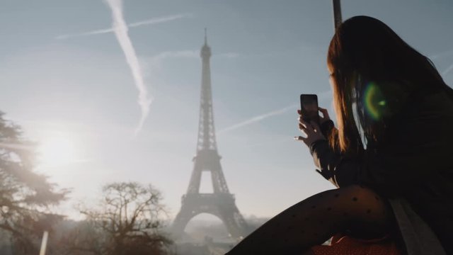 Happy young tourist woman taking smartphone photo of sunset Paris Eiffel Tower panorama on romantic vacation slow motion