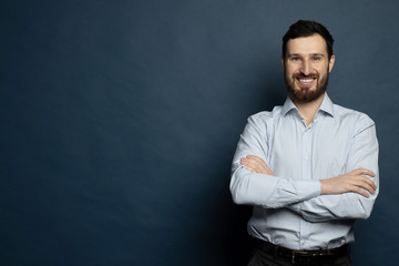 Happy young man. Portrait of handsome young bearded man keeping arms crossed and smiling.