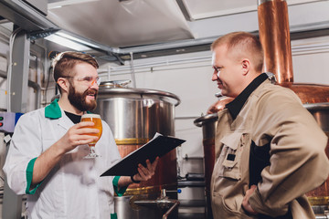 Mature man examining the quality of craft beer at brewery. Inspector working at alcohol manufacturing factory checking beer. Man in distillery checking quality control of draught beer.