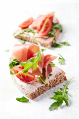 Tasty sandwiches with cream cheese, smoked ham and fresh herbs. Bright wooden background. 