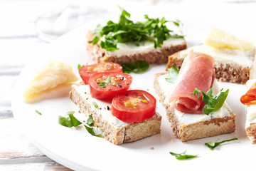 Fototapeta na wymiar Tasty Sandwiches with cherry tomatoes, ham, cream cheese and rocket. Bright background. 