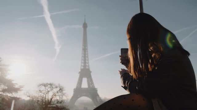 Happy young tourist woman taking a photo of epic sunset Paris Eiffel Tower sky panorama with smartphone slow motion.