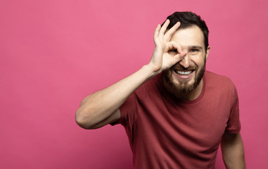 Portrait of a handsome young bearded man laughing on pink background.