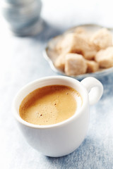 Cup of coffee and brown sugar cubes on bright wooden background. Close up. 