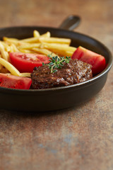 Fried hamburger steak with tomatoes and french fries. Rustic background. 