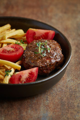 Fried hamburger steak with tomatoes and french fries. Rustic background. 