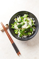 Cooked rice with fried broccoli on bright stone background. Top view. 