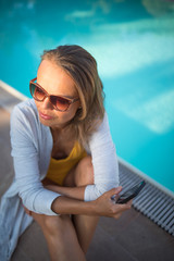 Young Beautiful Suntanned Woman wearing sunglasses relaxing next to a Swimming Pool  on a lovely Summer Day