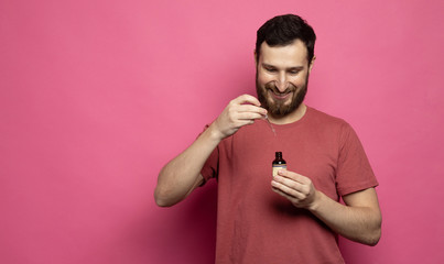 Close up image of handsome bearded man with pipette with beard oil on pink background.