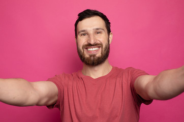 Obraz premium Close up portrait of a cheerful bearded man taking selfie over pink background.