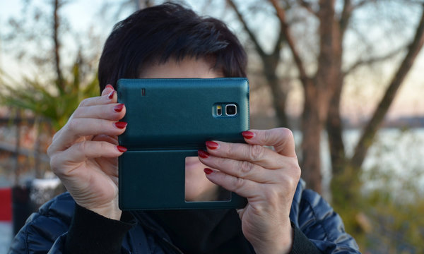 A woman takes pictures on a smartphone that is holding in her hands with a red manicure.