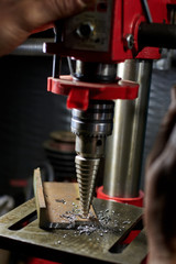 Hands of a man who drills a metal part on a machine tool.
