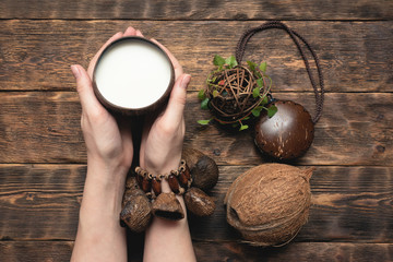 Coconut milk in cup and coconut in female hands on brown wooden table background.