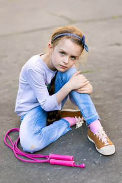 Frightened youg girl sitting on the pavement with skipping rope looking towards camera