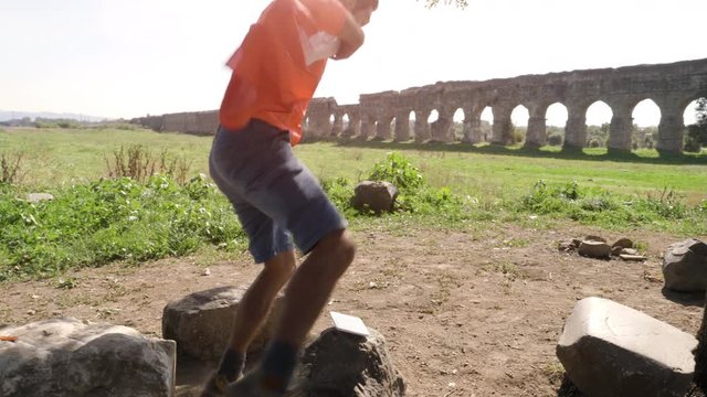 Young man in orange sportswear wearing italian flag as cape watches football match on smartphone and exults running in front of ancient roman aqueduct in parco degli acquedotti in rome at sunset