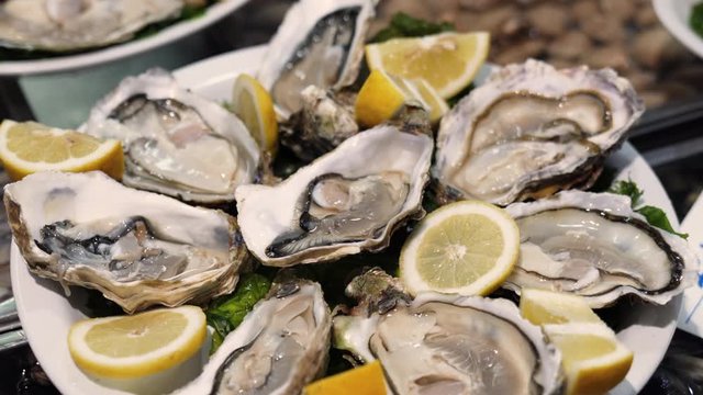 Expensive oysters on fish market counter. Fresh delicious delicacy with lemon and ice. Close-up of fresh oysters on market