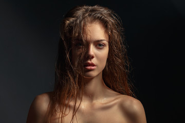 Fototapeta premium Beauty portrait of a young attractive girl with wet hair on a dark background.