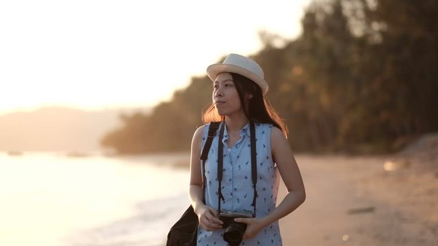 Asian woman walking along beach and take a photo with her camera.