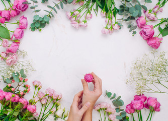 Frame of flowers near female hands holding rose flower on marble background