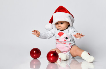 Smiling baby toddler playing with christmas tree red glass balls rolling on the floor