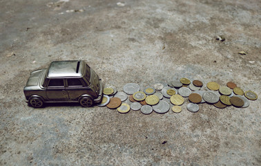 metallic car money box moving with a line of coins behind on the road- image symbol of losing or wasting money