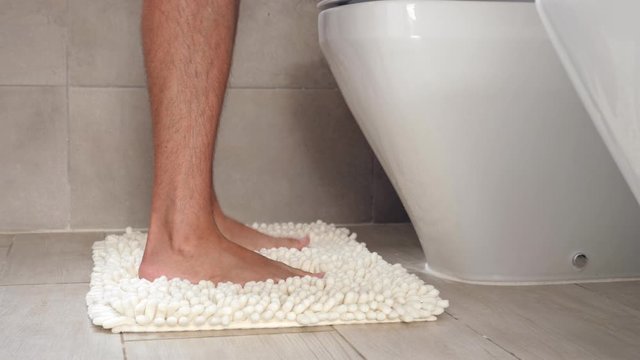 Man sitting on wc toilet bowl at the bathroom and holding a toilet paper roll, no face