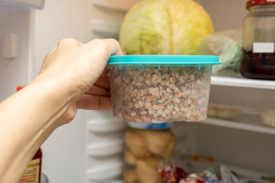 A hand of a dieting woman taking a plastic container with cooked buckwheat from a frige, freezer, losing weight concept
