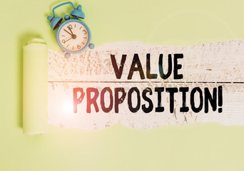 Writing note showing Value Proposition. Business concept for innovation service intended make product attractive Alarm clock and torn cardboard on a wooden classic table backdrop