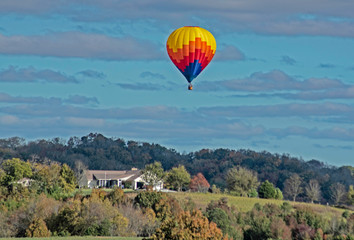 Naklejka premium A single hot air balloon flies over a green valley.