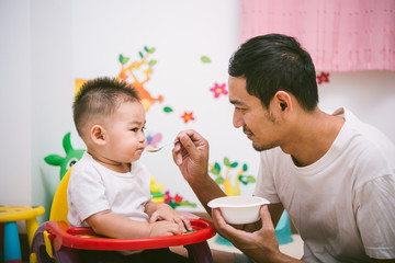 Father acting Mom feeding his son baby 1 year old on chair