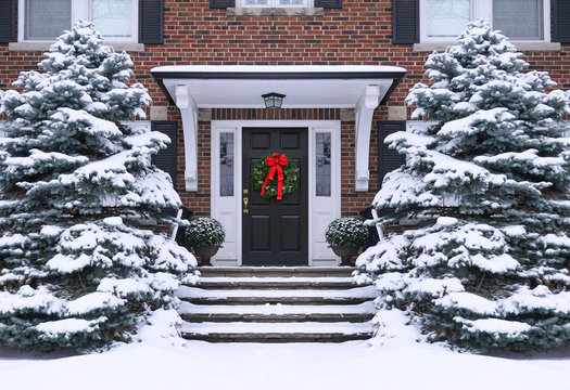 Front door of  house with Christmas wreath and snow covered pine trees