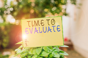Writing note showing Time To Evaluate. Business concept for judge something with respect to its worth or significance Plain paper attached to stick and placed in the grassy land