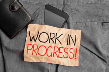 Writing note showing Work In Progress. Business concept for unfinished project that still added to or developed Smartphone device inside trousers front pocket with wallet