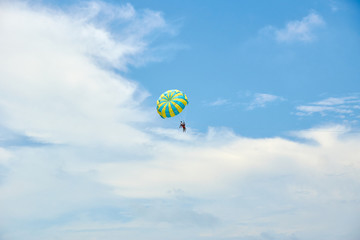 People are flying on a parachute against a blue sky with clouds.