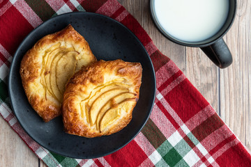 Fresh individual apple tarts on a black plate, cup of milk, red, green, and white cloth napkin, wood background