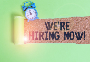 Conceptual hand writing showing We Re Hiring Now. Concept meaning recently employ someone or pay someone to do particular job Alarm clock and torn cardboard on a wooden classic table backdrop