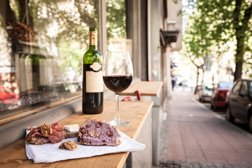 Glass and bottle of French red wine on display on the table of a terrace of Paris with slices of baguette bread, brie cheese and saucisson (a cured meat from France) for appetizers